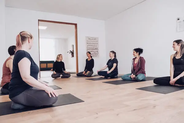 Teilnehmer der Yogaausbildung mit Yoga-Bergisches-Land, die auf Yoga-Matten sitzen und von einer Lehrerin angeleitet werden.
